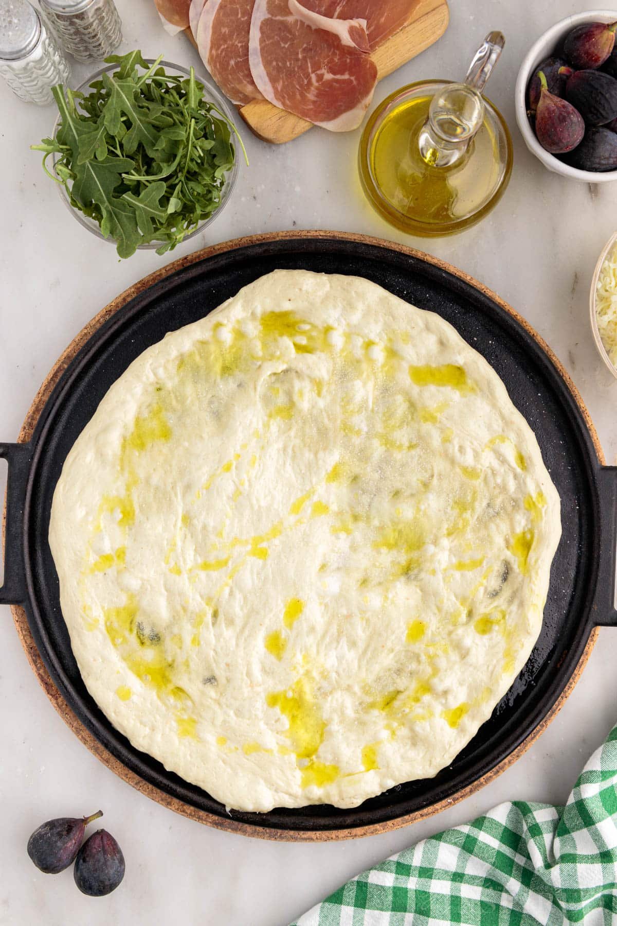 Pizza dough on cast iron pizza pan, drizzled with olive oil.