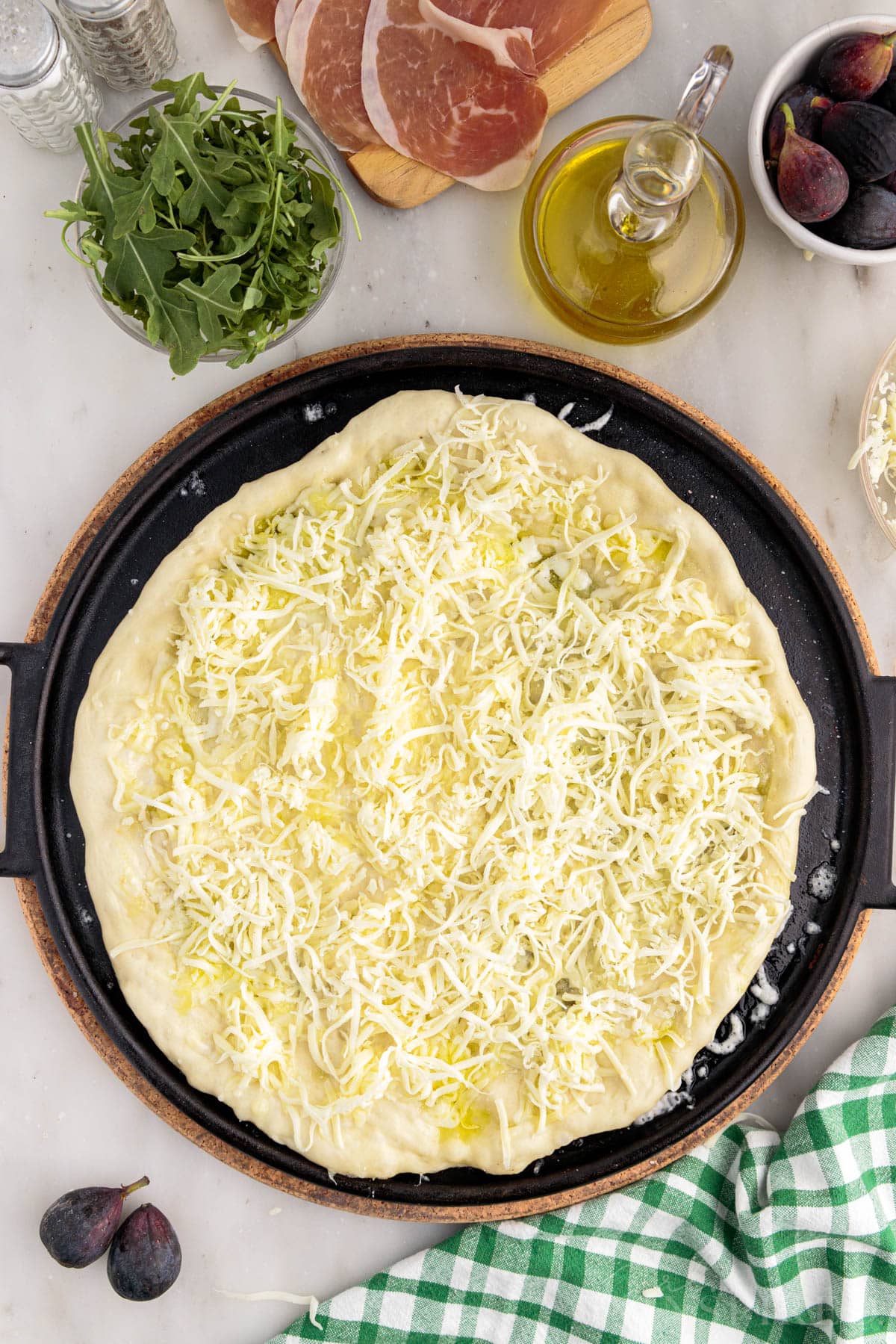 Cheese sprinkled over pizza dough on cast iron pizza pan.