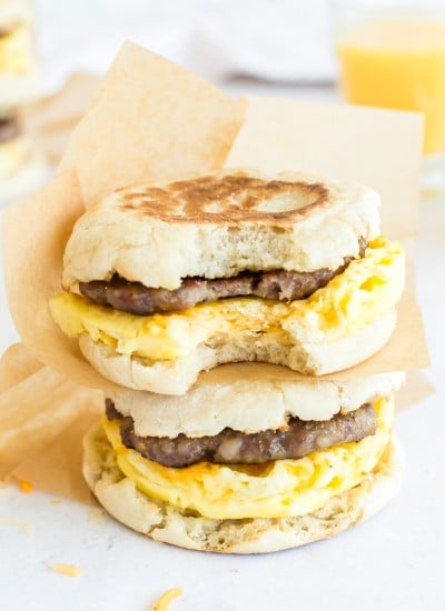 two stacked breakfast sandwiches with parchment wrappers and bite taken from one