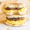two stacked breakfast sandwiches with parchment wrappers and bite taken from one