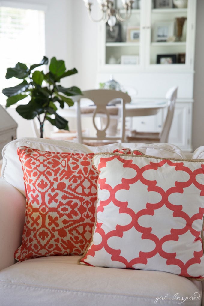 coral and white pillows on white couch with kitchen table and hutch in background