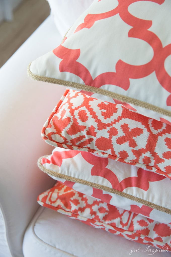 close up of coral and white patterned pillows stacked on white couch