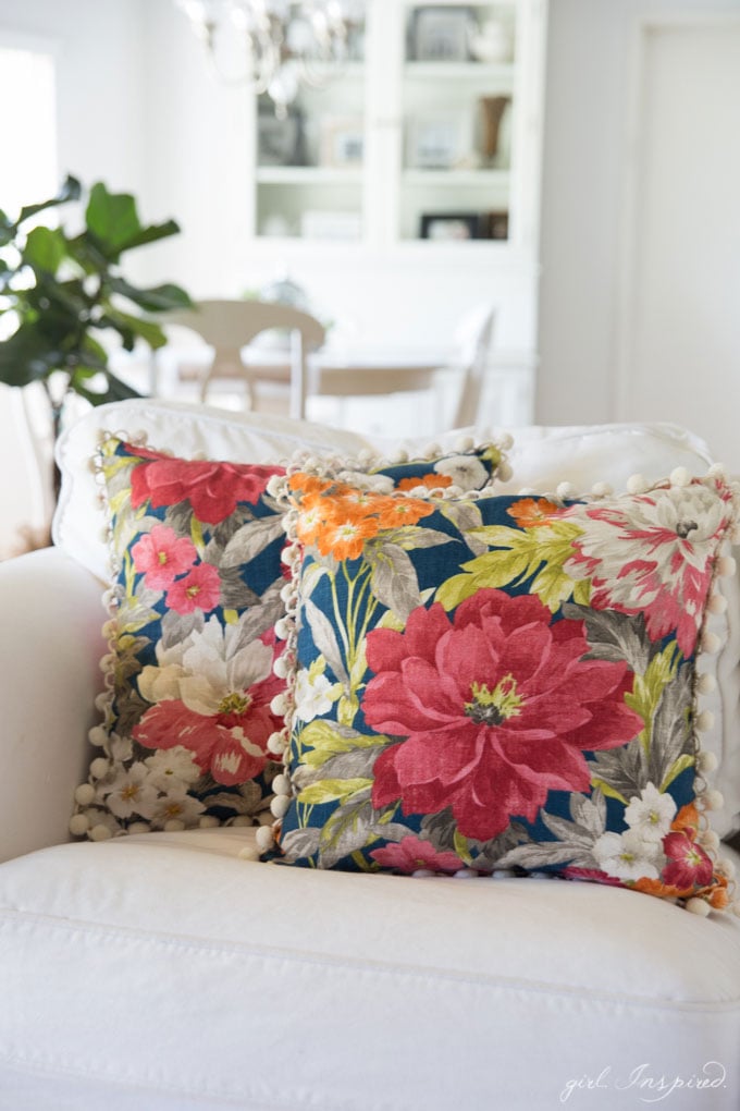 two blue floral pillows on white couch with kitchen table and hutch in background