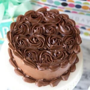 Cake with rosettes of dark chocolate buttercream on cake stand in front of gifts.