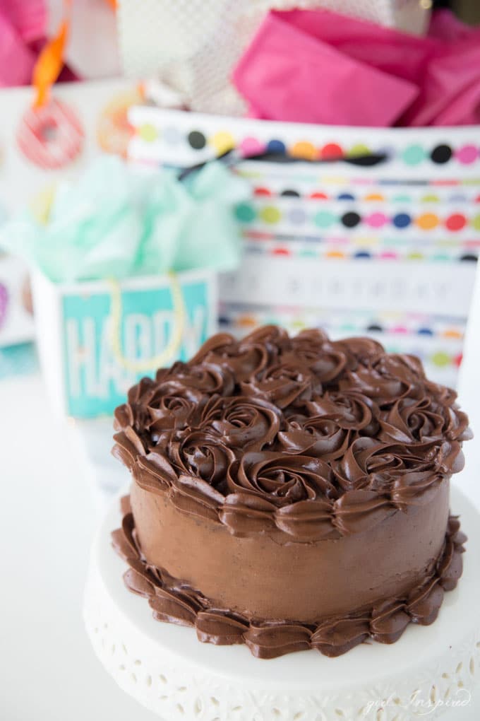 dark chocolate frosting piped in swirls on cake on white platter with birthday gift bags in background