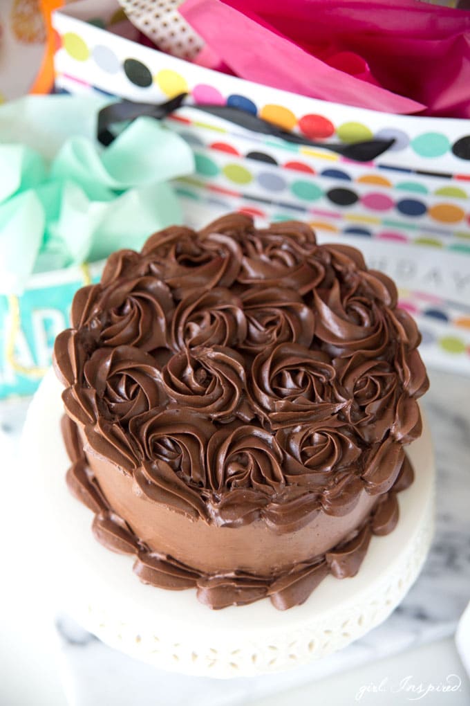 dark chocolate frosting piped in swirls on cake on white platter with birthday gift bags in background