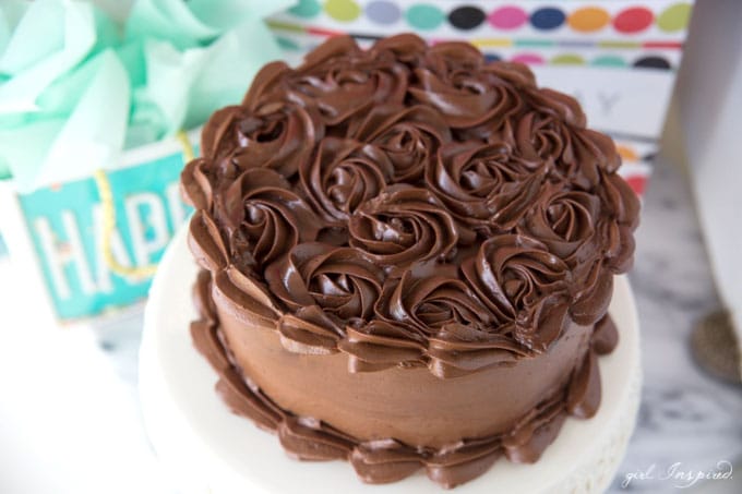 dark chocolate frosting piped in swirls on cake on white platter with birthday gift bags in background