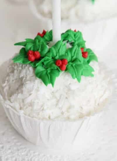 Snowball ice cream with icing wreath around the top and candle in the center, in a paper cup.