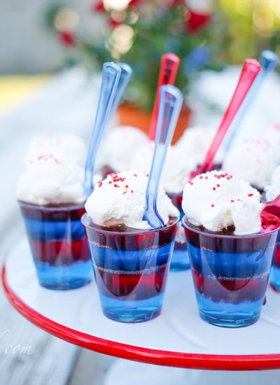 blue and red jello cups with whipped cream on white and red cake platter on outdoor table