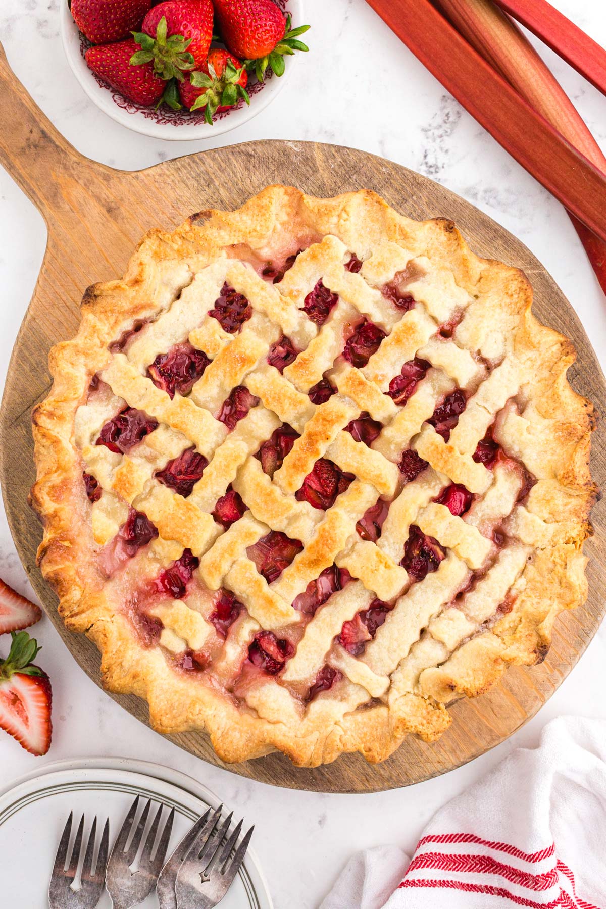Baked strawberry rhubarb pie with lattice crust on a wooden board.
