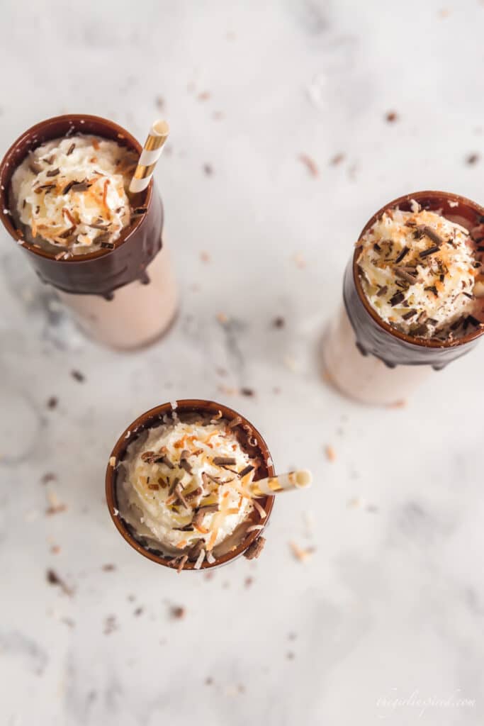 overhead photo of coconut rum cocktails showing whipped cream and coconut topping on chocolate drizzled glasses