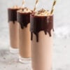 three tall glasses with chocolate dripping from rim, filled with chocolate milk and liquor and topped with whipped cream and gold stripes straws