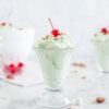 Watergate Salad in glass ice cream dishes with three maraschino cherries and pecans on top