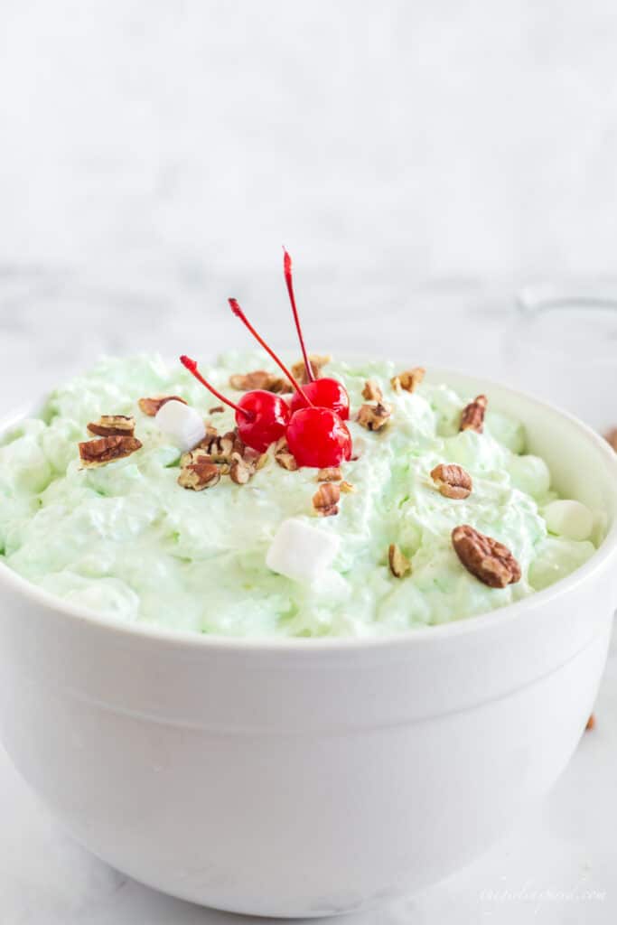 Watergate Salad in white bowl with three maraschino cherries and pecans on top