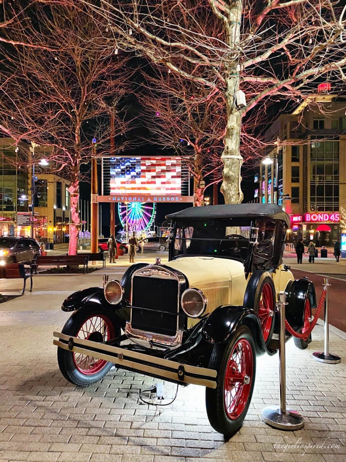 Nighttime view of old Ford truck on street display with statues, trees, and illuminated American flag in the background.