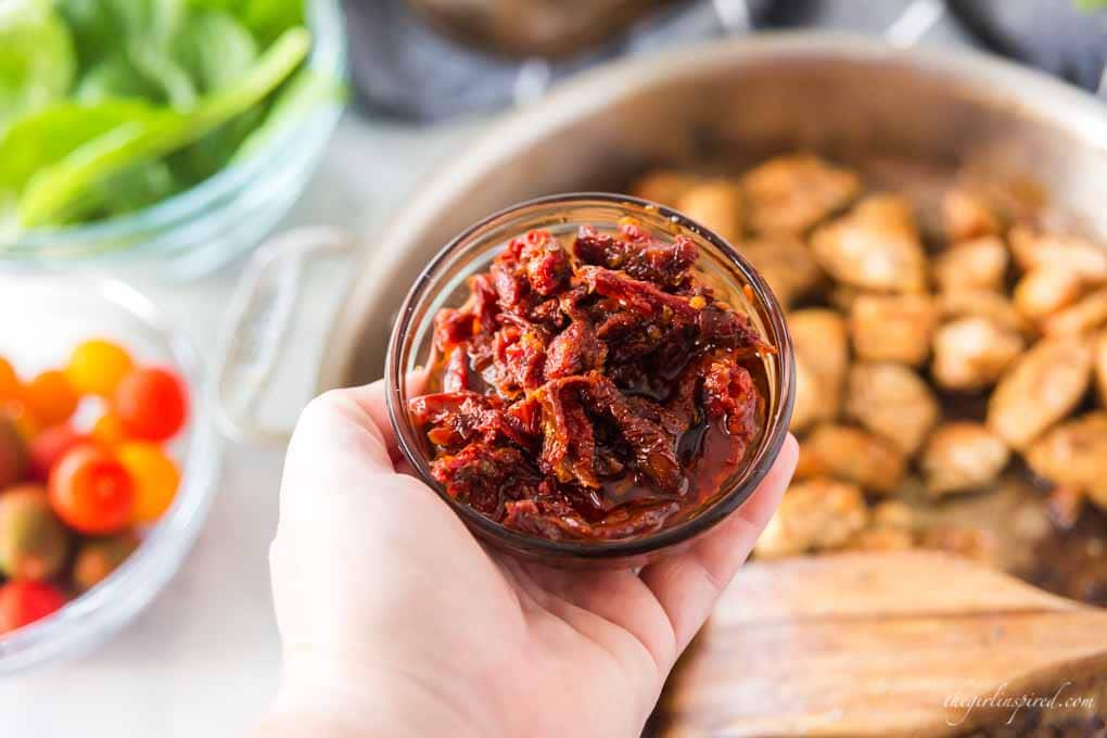 glass dish of sun-dried tomatoes with browned chicken, spinach, and tomatoes in background