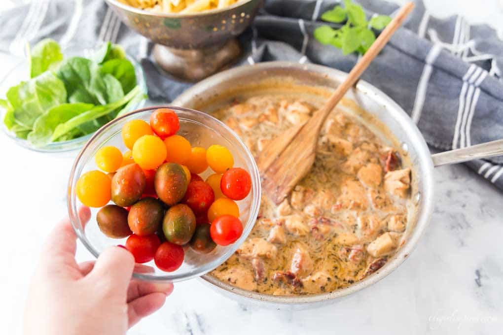 Bowl of cherry tomatoes with chicken, saucepan, and pasta in the background