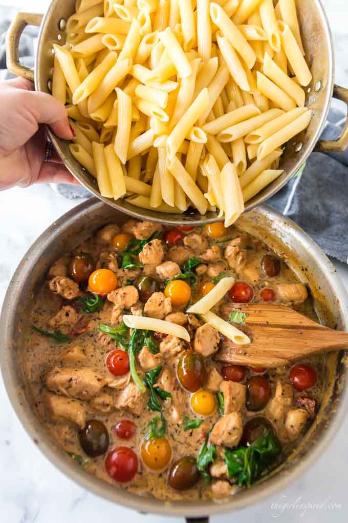 penne pasta pouring into chicken and tomato saucepan mixture