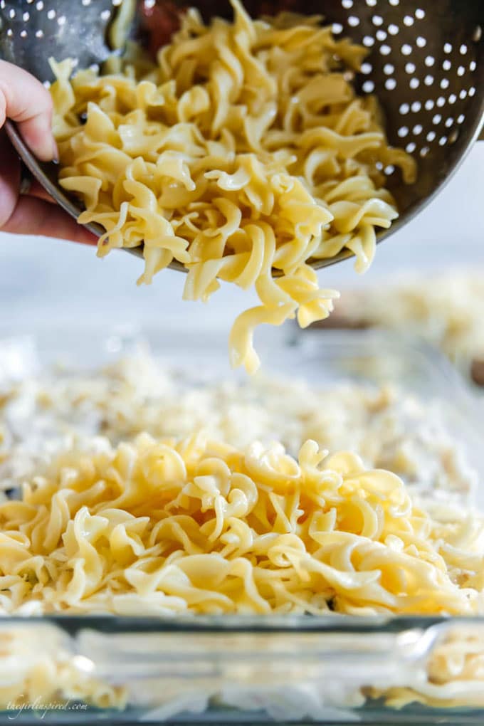 noodles being poured from colander into glass casserole dish