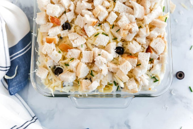 uncooked tuna casserole in glass baking dish with kitchen towel and sliced olives on countertop