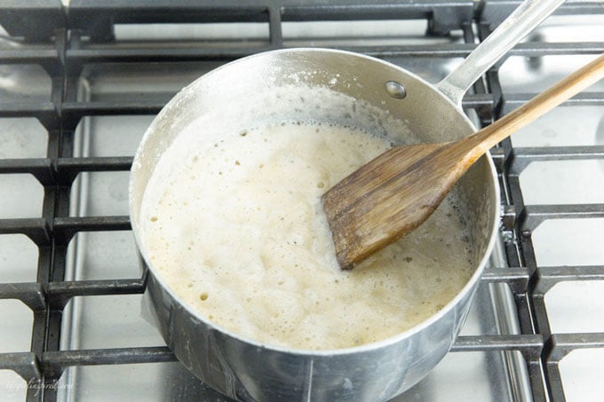 wooden spoon stirring white sauce in saucepan over stovetop
