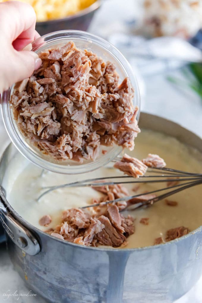 tuna being added into saucepan with white sauce