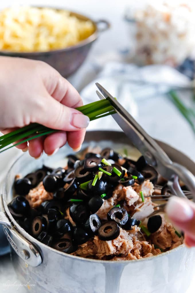 scissors being used to cut chives into saucepan with tuna and olives