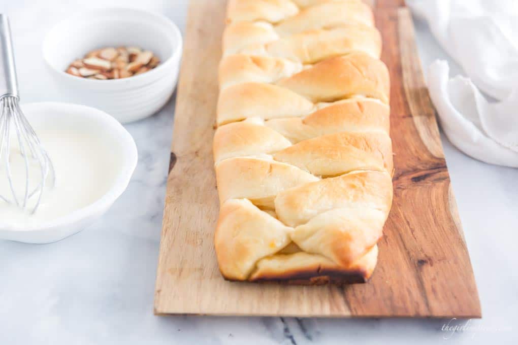 baked sweet bread on cutting board with white bowls of almonds and icing
