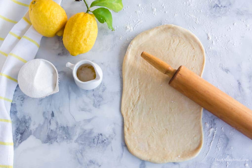 rolled out dough with lemons and rolling pin on marble counter