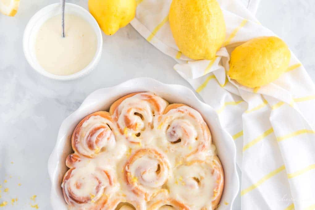 baked sweet rolls in white pie plate, with white dishes, lemons, and dish towel in background