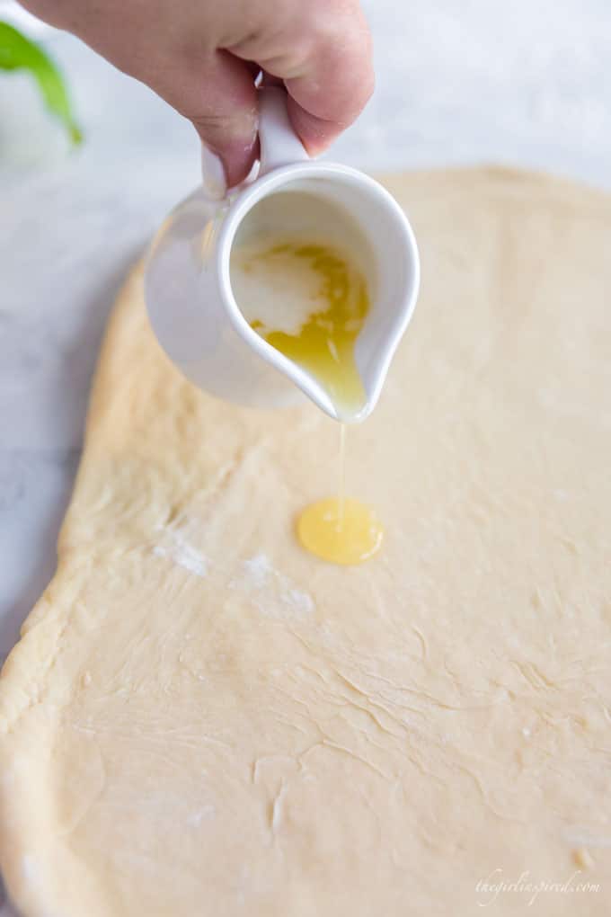 butter pouring from white crock onto rolled out sweet dough