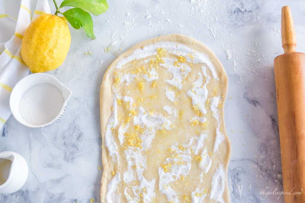 rolled out dough with sugar and lemon zest, lemons, white dishes, and rolling pin on counter