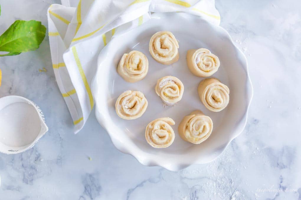 sliced lemon rolls in white pie plate with yellow and white dish towel
