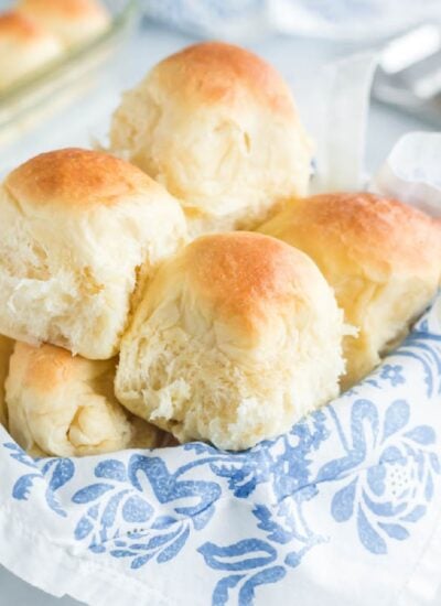Pile of sweet dinner rolls in a bread basket with a floral linen.