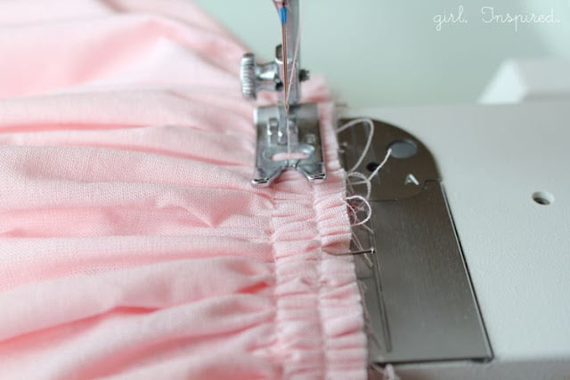 close up of sewing machine foot sewing over pink fabric gathers