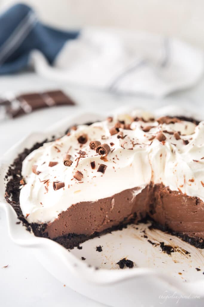 photo of partially cut chocolate cream pie in white pie plate with blue towel in background