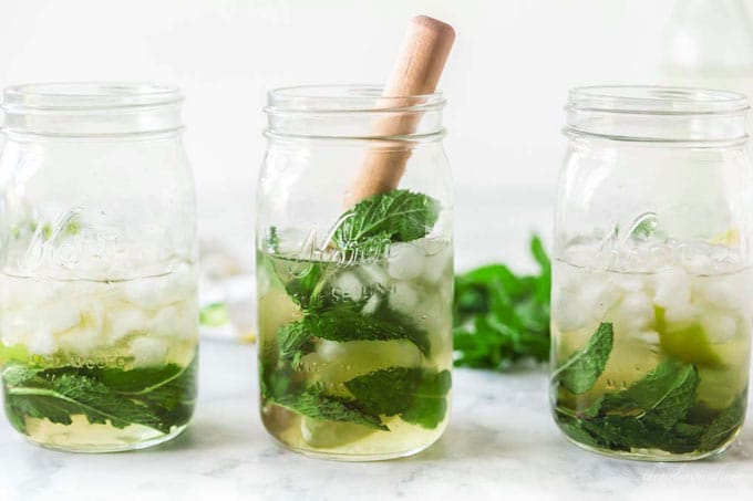 three mojitos in mason jars garnished with lime, mint, and bamboo straws
