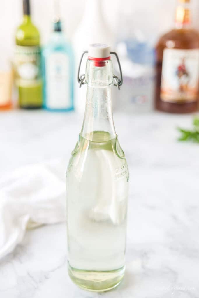 tall glass bottle of simple syrup with other alcohol bottles in the background