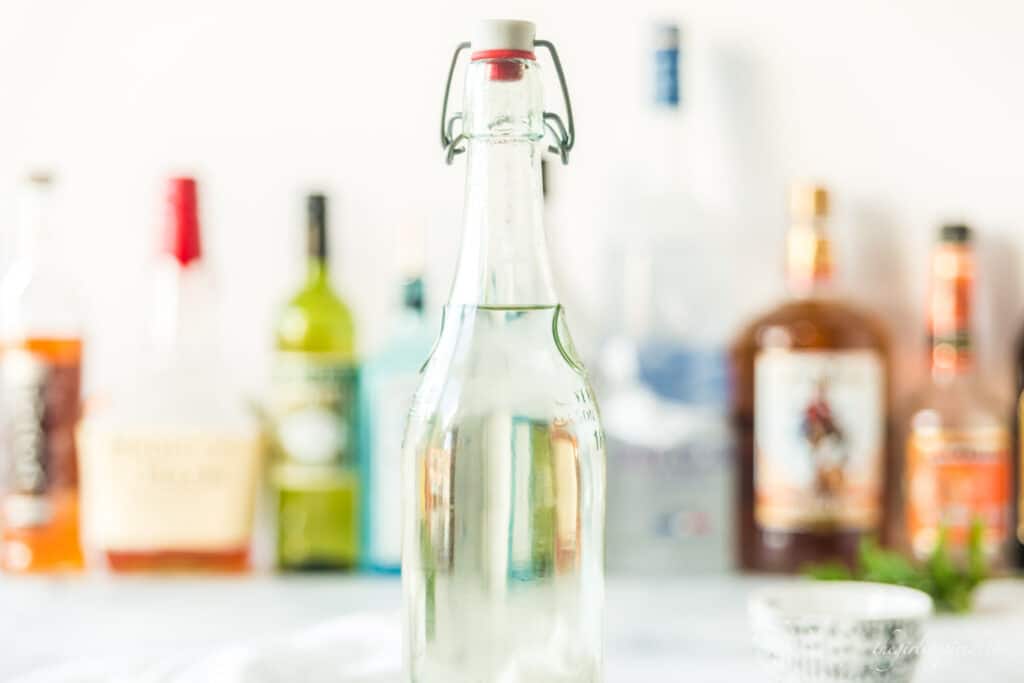 tall glass bottle of simple syrup with other alcohol bottles in the background