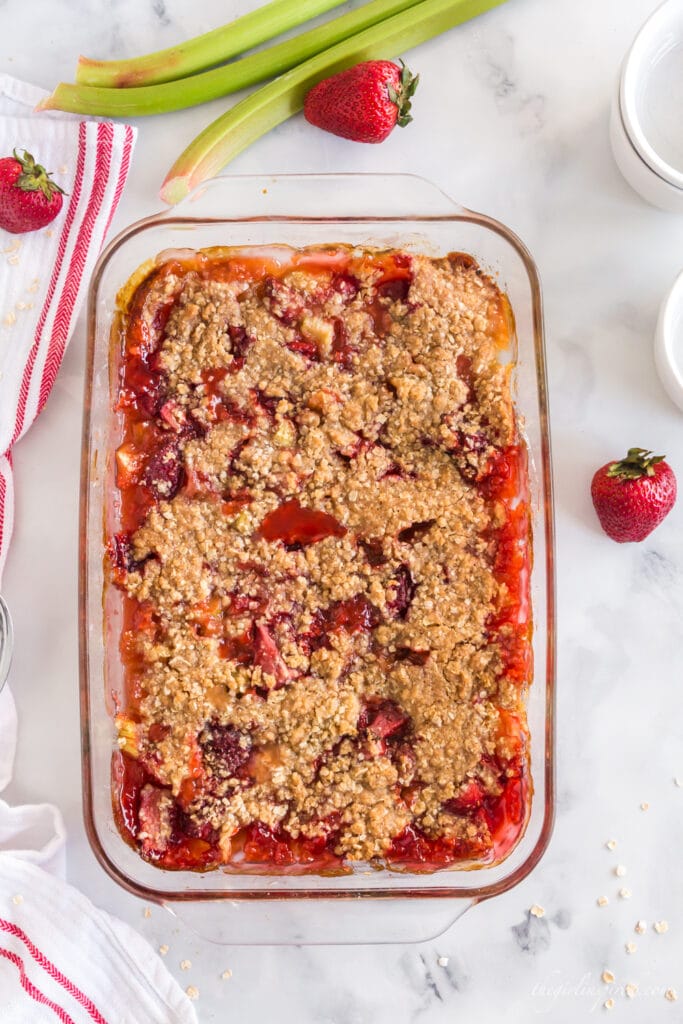 Baked Strawberry Rhubarb Crisp in glass dish with fresh strawberries and rhubarb and red and white linen