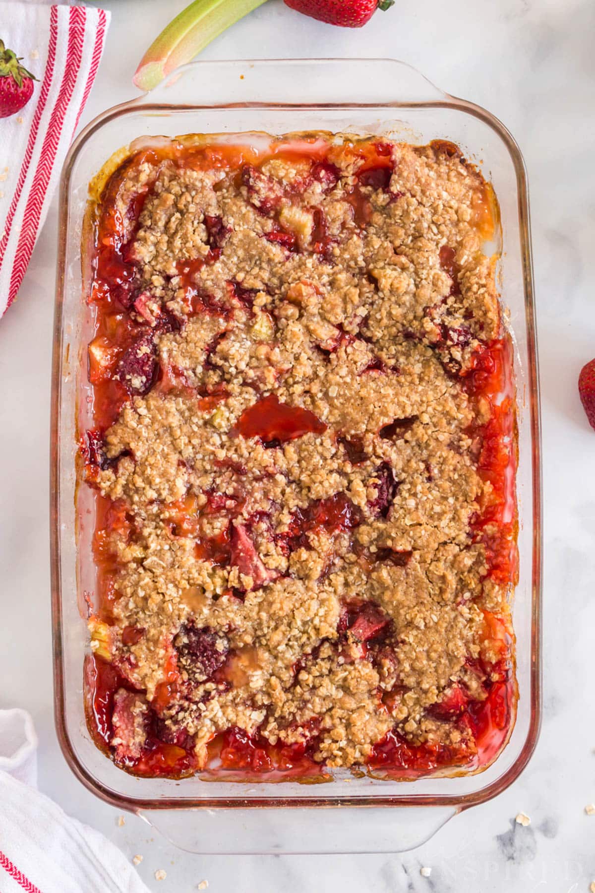 Baked Strawberry Rhubarb Crisp in glass dish with fresh strawberries and rhubarb and red and white linen