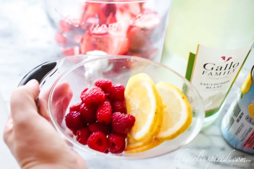 measuring cup with raspberries and lemon wedges, bottle of white wine in background