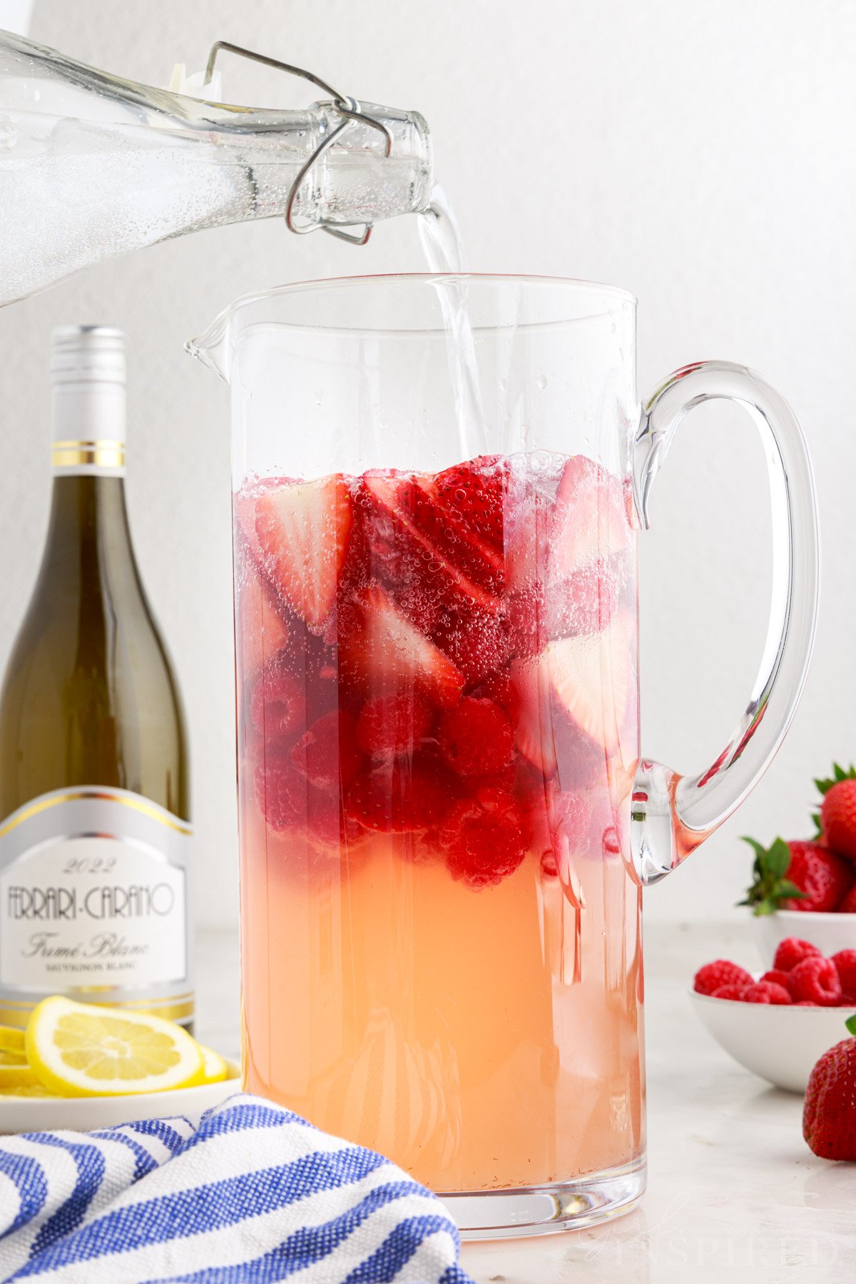 Club soda poured into pitcher with strawberry sangria and fruit.