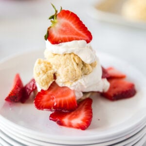 Biscuits, whipped cream, and fresh strawberries on a stack of white plates