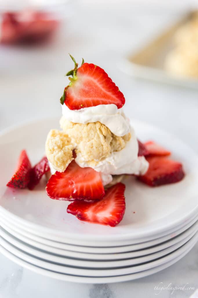 Biscuits, whipped cream, and fresh strawberries on a stack of white plates