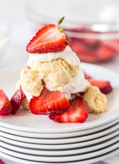 Strawberry shortcake biscuits, whipped cream, and fresh strawberries on a stack of white plates