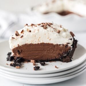 Slice of chocolate cream pie on a stack of white dessert plates.