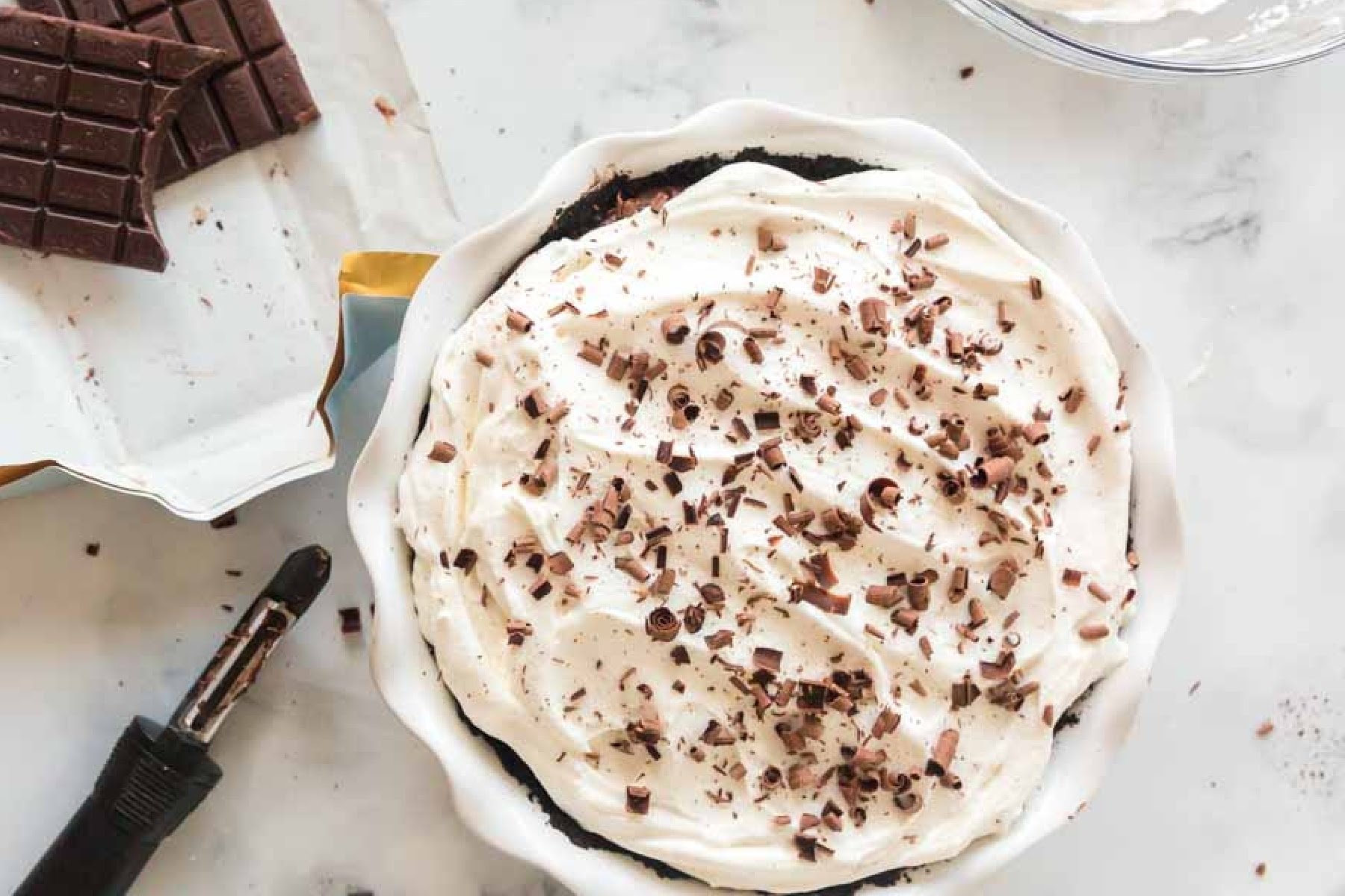 Chocolate bar, peeler, and chocolate curls over the top of chocolate cream pie.