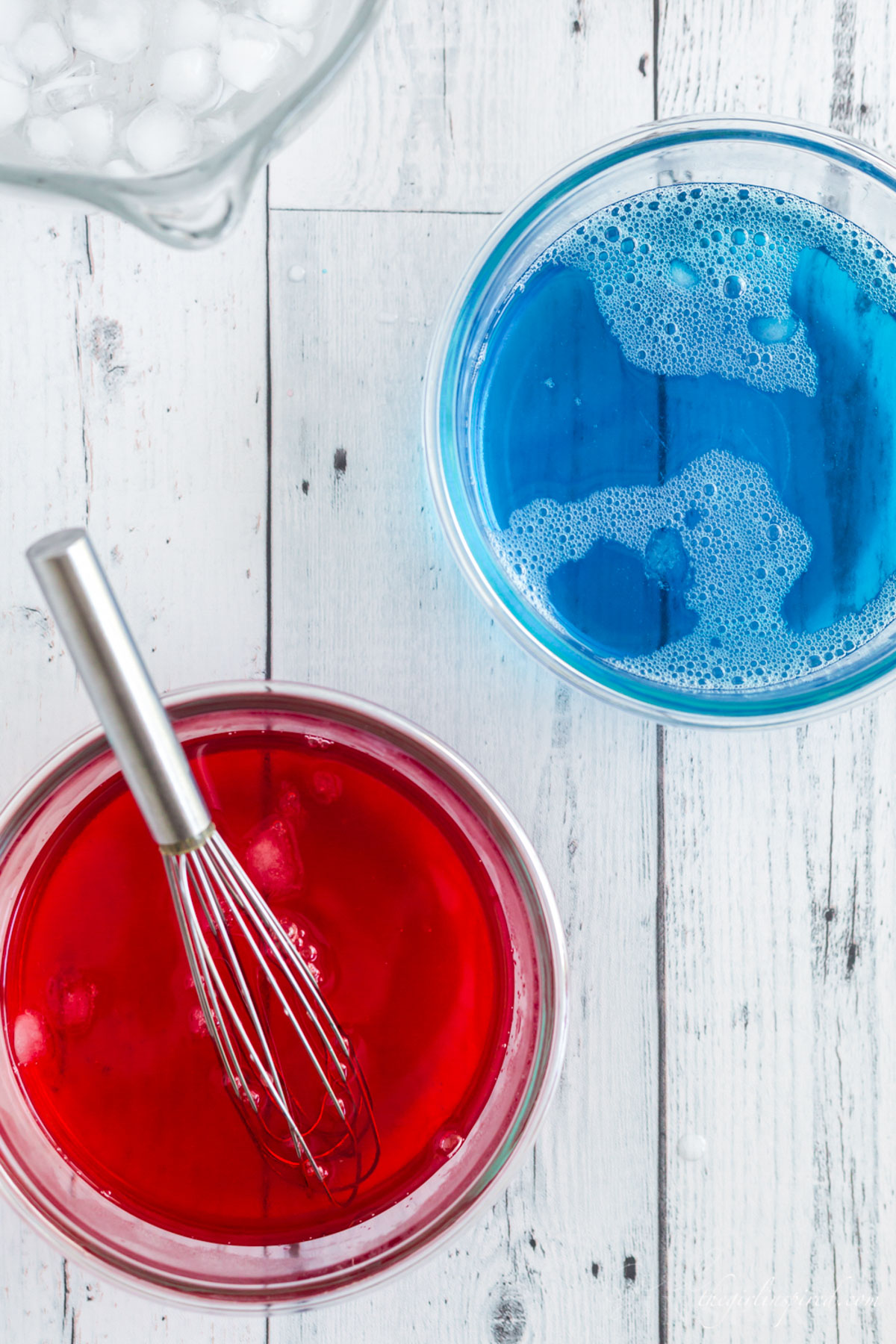 Red jello and blue jello liquid in glass bowls with whisk. Ice in bowls.