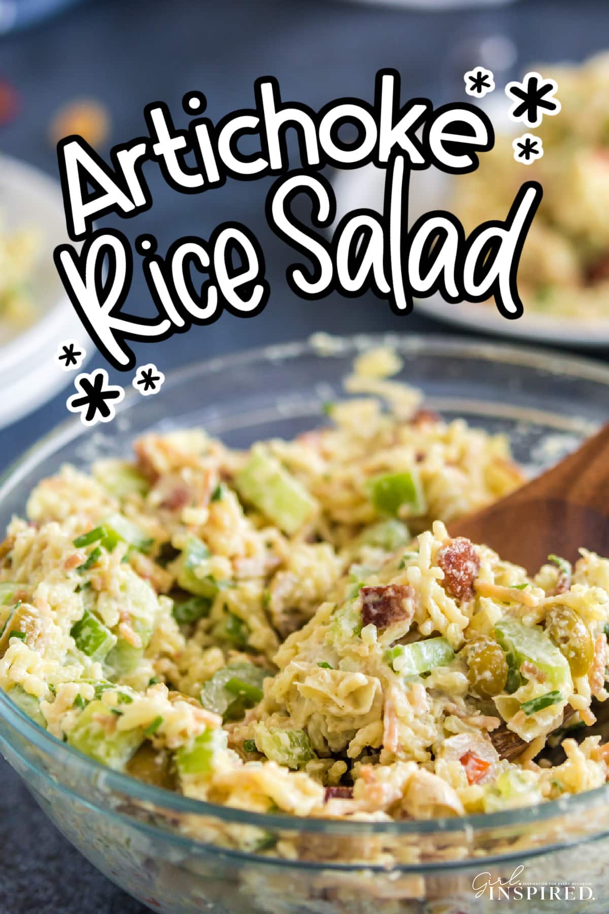 Glass bowl of artichoke rice salad with wooden spoon.